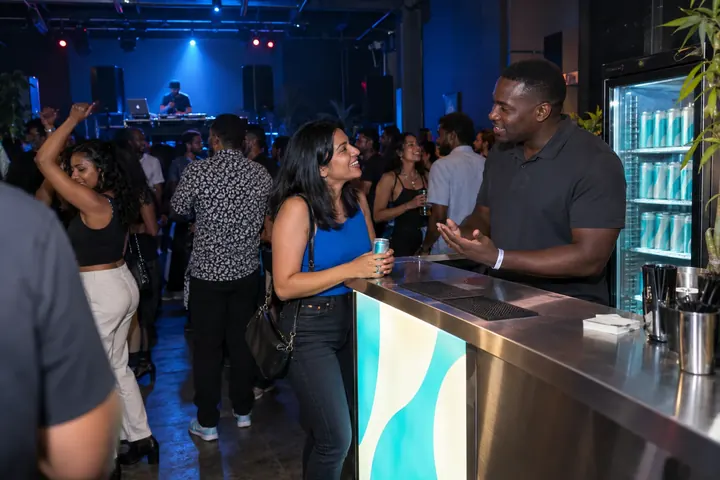 A beverage representative speaking with a guest at a blue-lit club bar